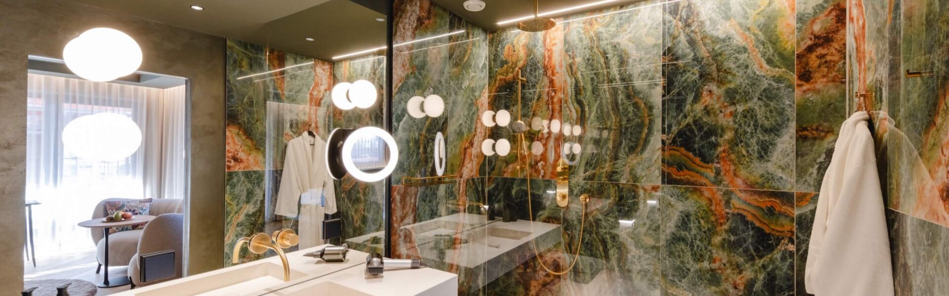 Modernes Badezimmer im Hotel nōa Schladming mit Natursteinwand, Regendusche und goldenen Armaturen.