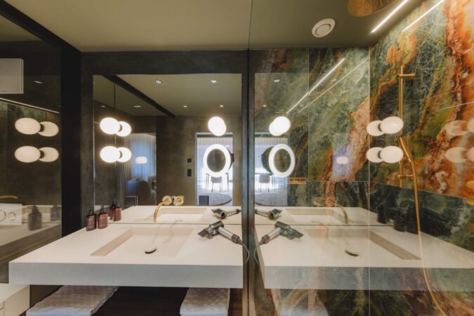 Waschbereich im Badezimmer des Hotel nōa Schladming mit Natursteinwand und goldenen Armaturen.