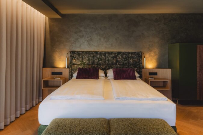 Modernes Doppelzimmer im Hotel nōa Schladming mit großem Bett und Waldmotiv-Kopfteil.