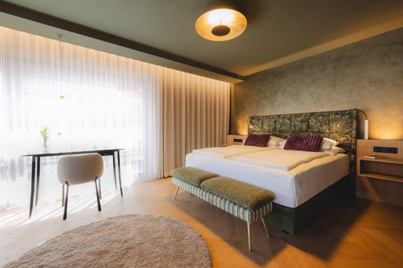 Design Suite im Hotel nōa Schladming mit Eichen-Fischgrätboden, Kunst-Headboard, Schreibtisch und großem Fenster.