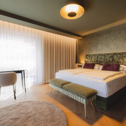 Hotel Schladming Design Suite im nōa Schladming mit Eichen-Fischgrätboden, Kunst-Headboard, Schreibtisch und großem Fenster.