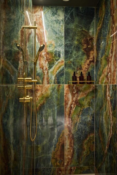 Regendusche mit goldenen Armaturen und grünem Naturstein in einer Suite im nōa Hotel Schladming.