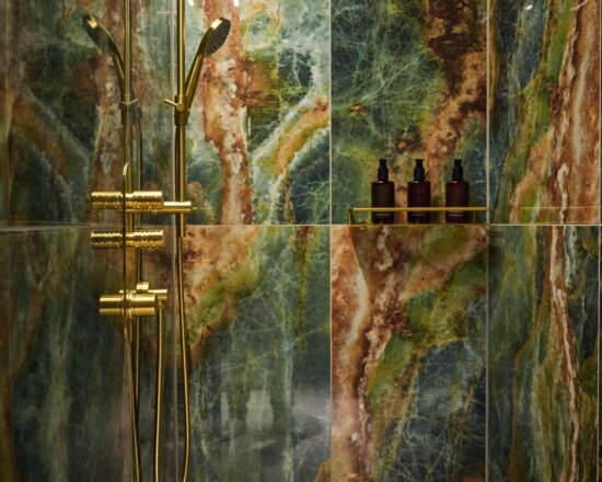 Regendusche mit goldenen Armaturen und grünem Naturstein in einer Suite im nōa Hotel Schladming.