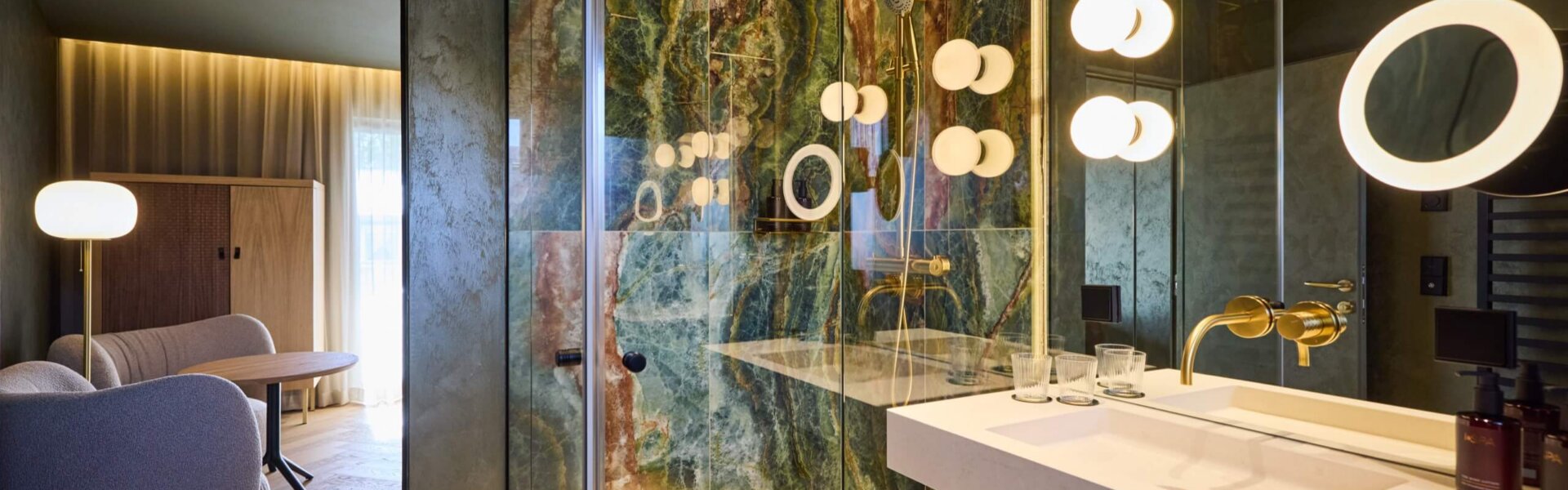 Luxuriöses Badezimmer im nōa Hotel Schladming mit Naturstein, goldenen Armaturen und moderner Regendusche