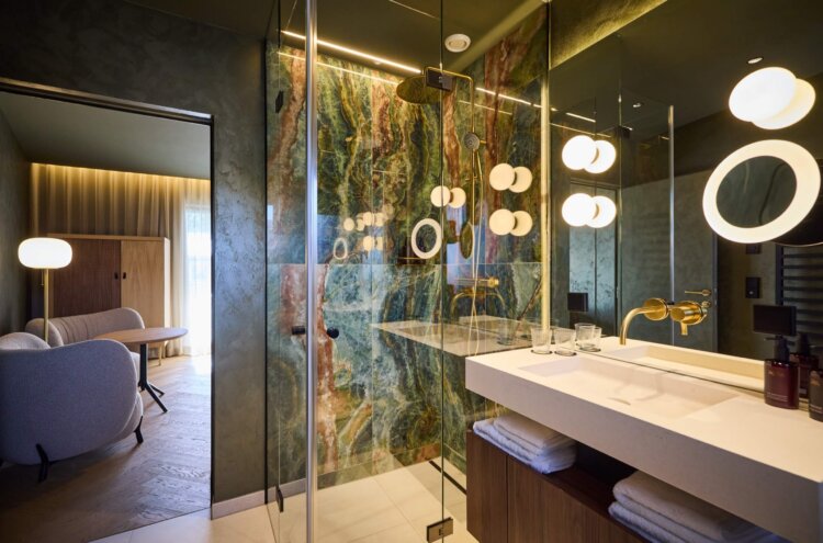 Luxuriöses Badezimmer im nōa Hotel Schladming mit Naturstein, goldenen Armaturen und moderner Regendusche
